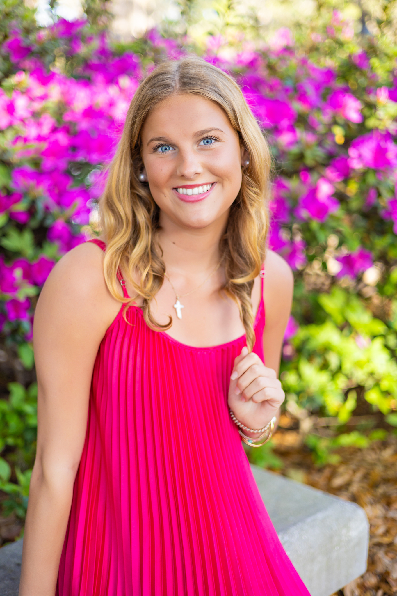 A high school grad sits on a garden bench smiling in a pink dress after visiting boutiques in Savannah
