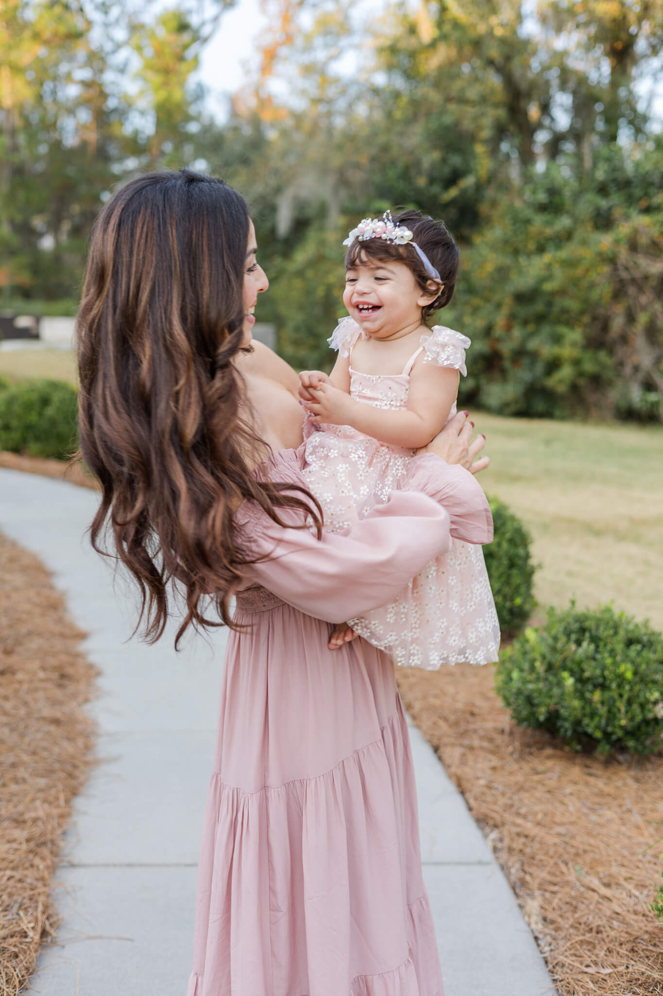 A baby girl giggles while sitting on mom's arms in a park sidewalk after visiting an indoor play space in Savannah