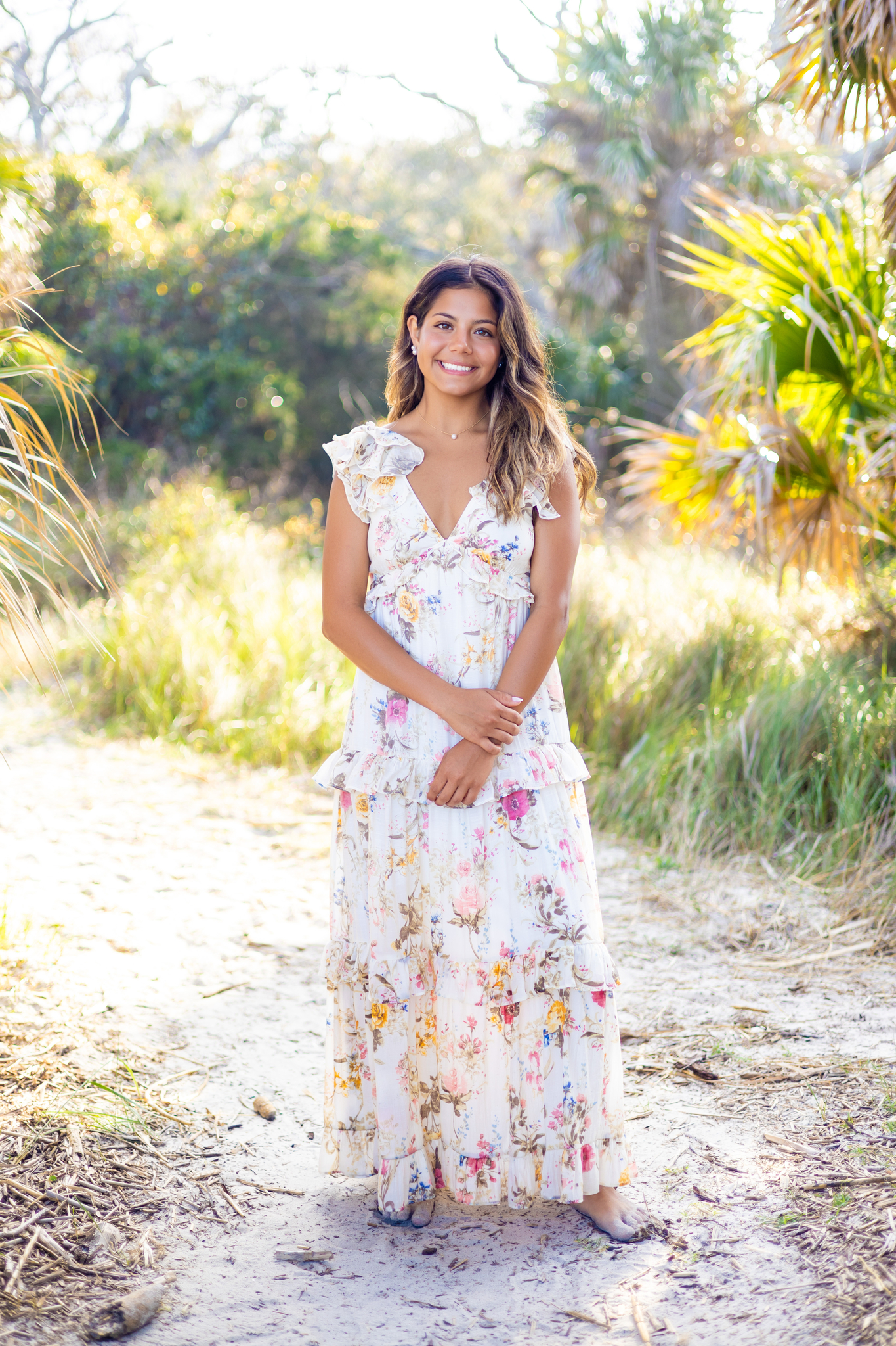 A happy graduate in a floral print dress stands in a beach dune path smiling