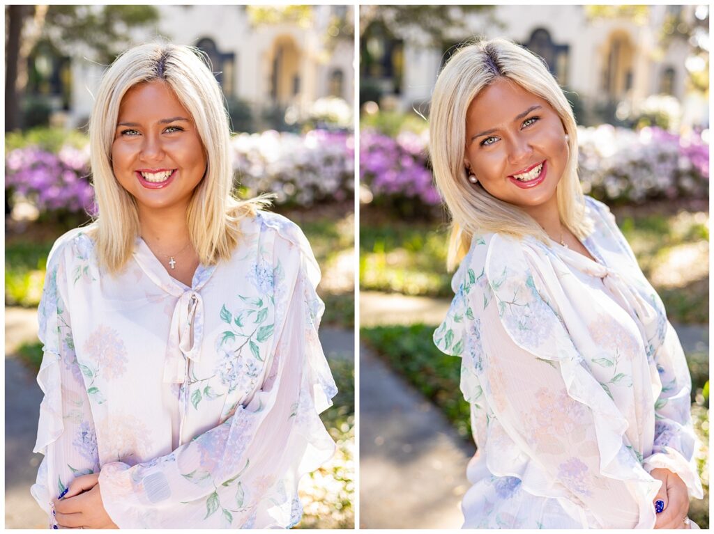 High school senior girl smiling in a soft floral blouse, posing in front of blooming azalea bushes with warm sunlight during a spring senior photo session in Savannah, GA.