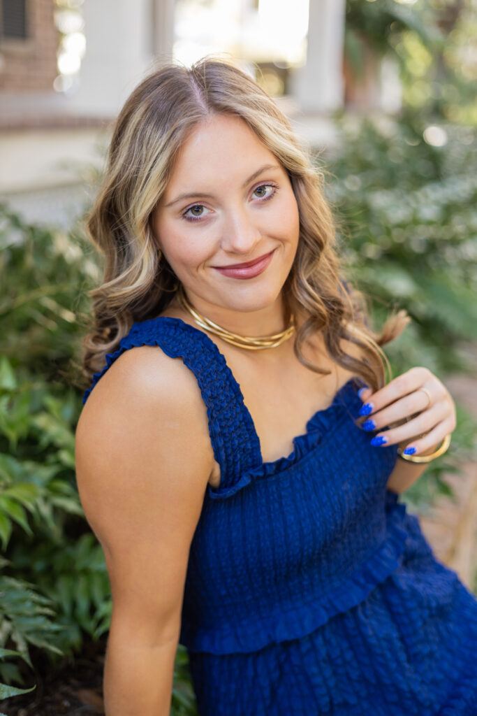 A high school senior in a blue dress sits in a garden smiling after finding great tutors in Savannah