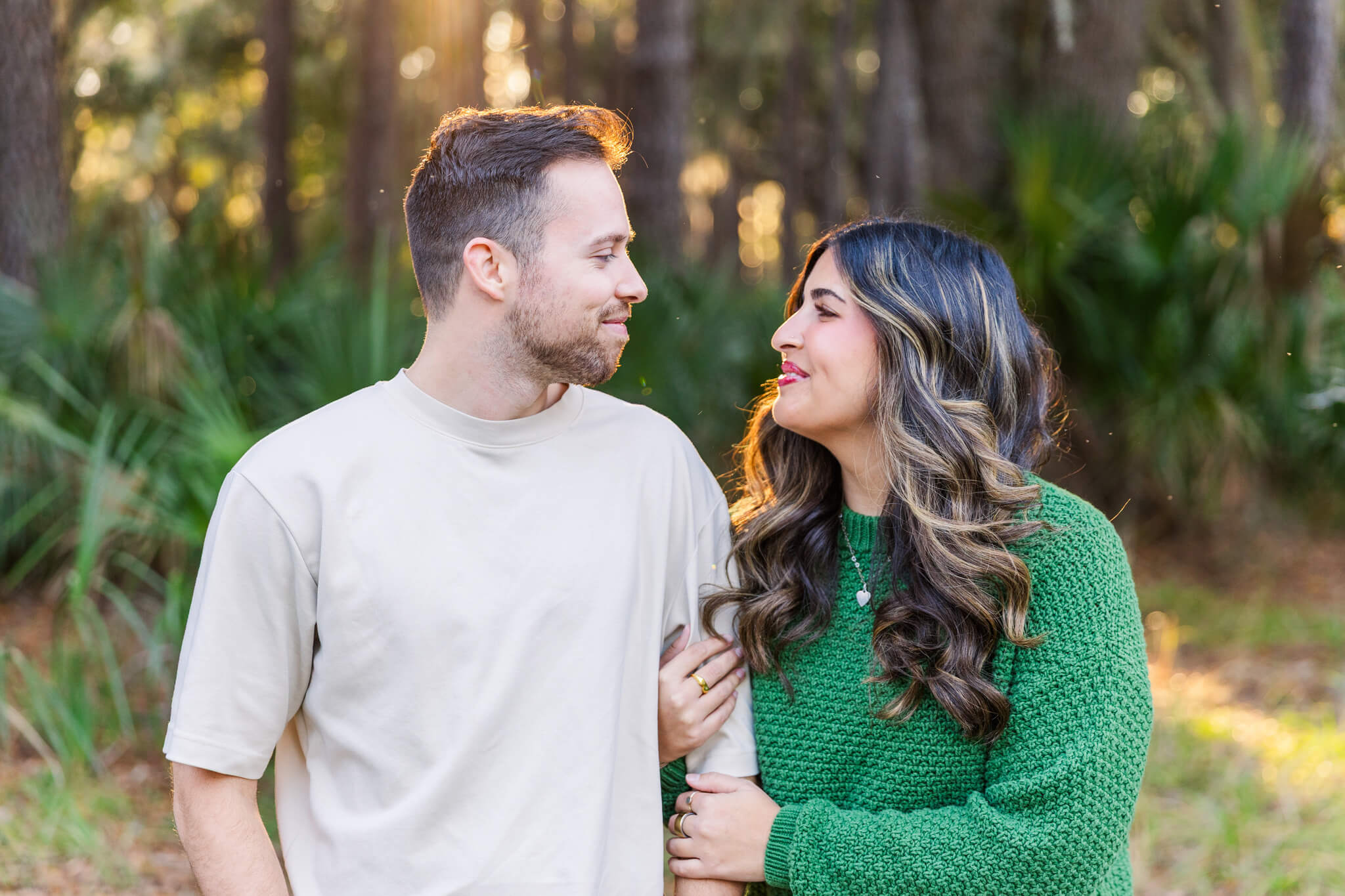 happy couple in tan and green smile at each other in a park at sunset
