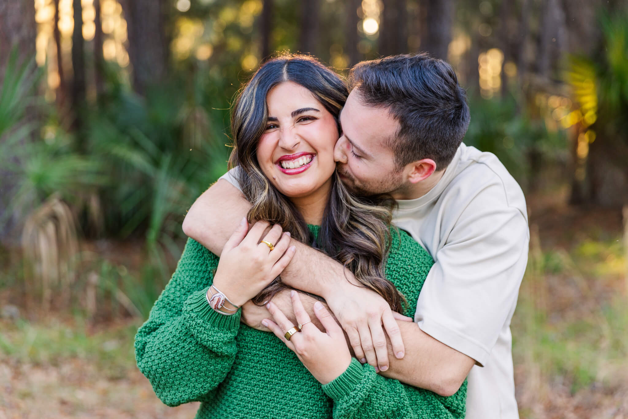 A woman in a green sweater is hugged and kissed from behind by her fiancee after enjoying date ideas in savannah