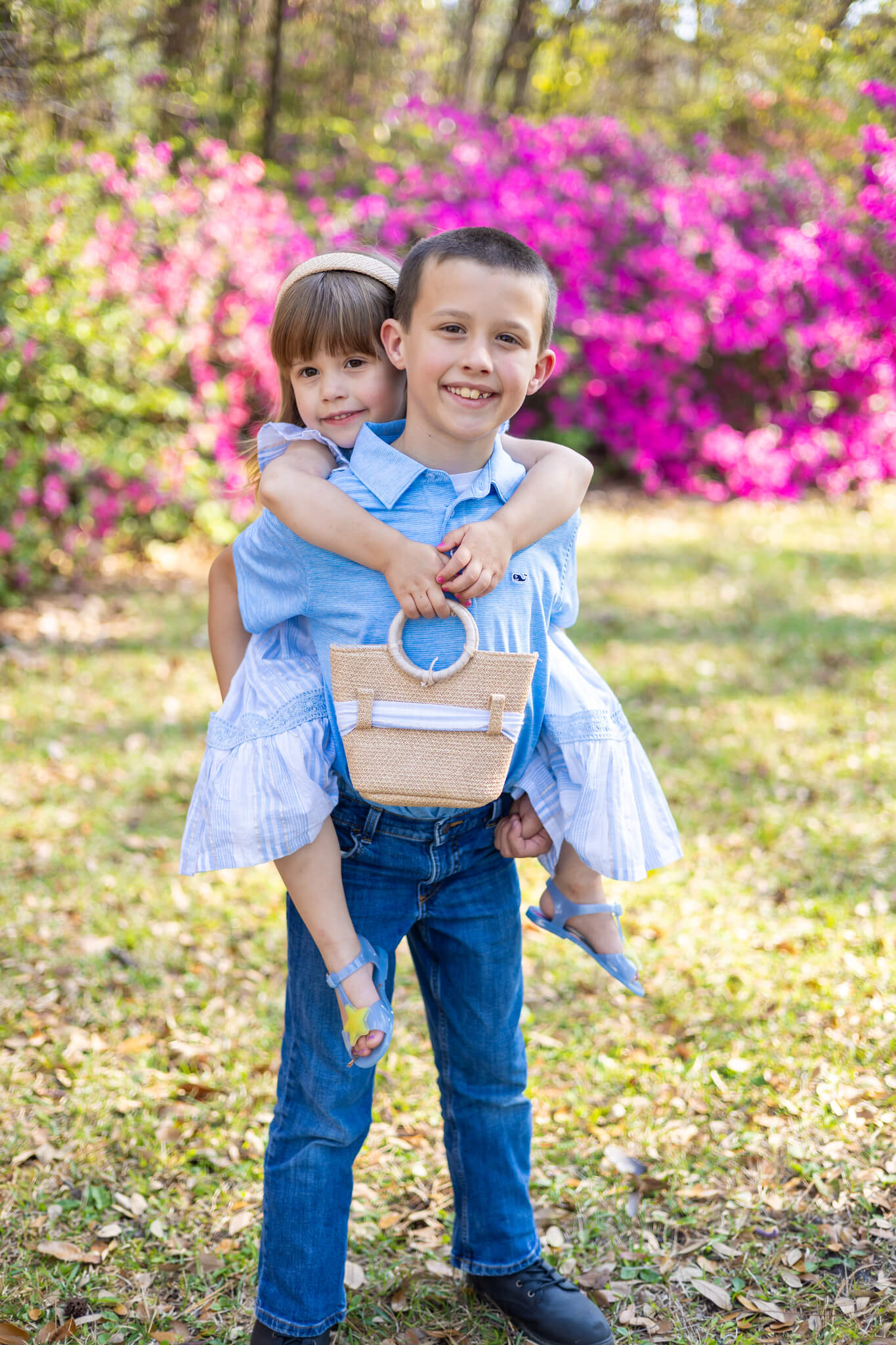 A toddler boy in a blue shirt carries his younger sister in a blue dress on his back in a park in fall after finding a nanny in savannah ga