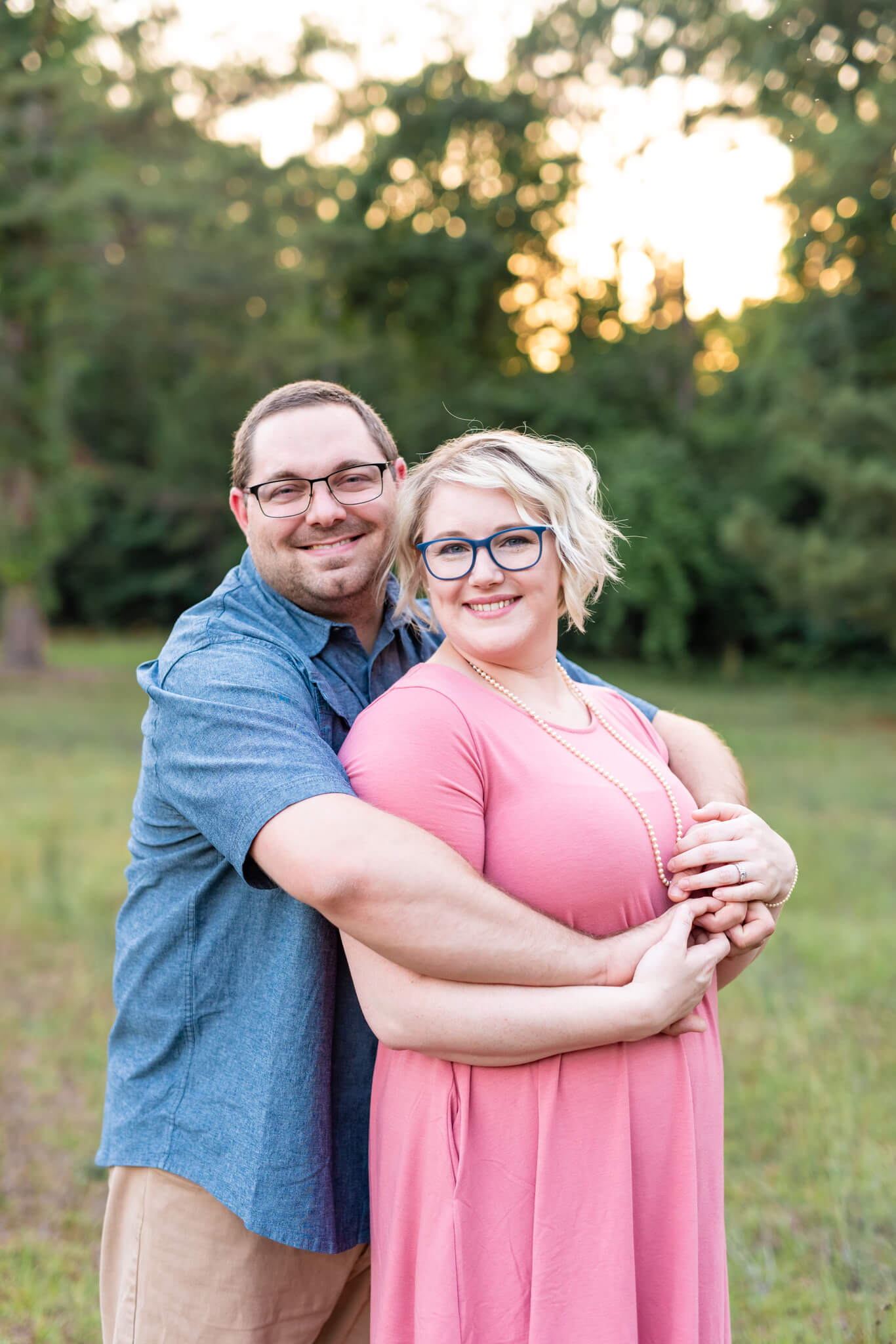 A happy couple snuggles in a pink dress and blue shirt in a park at sunset before heading out to nightlife in savannah