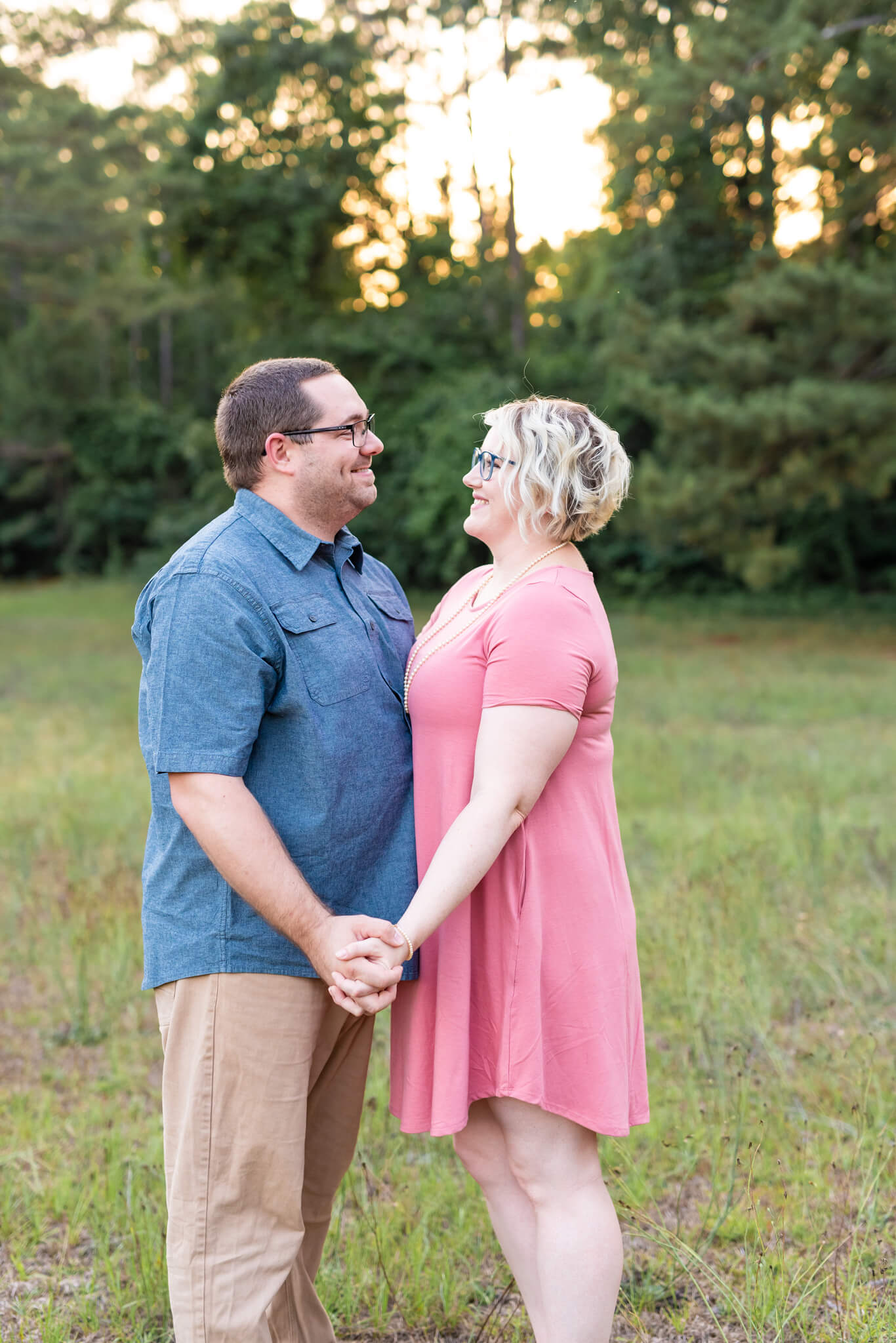 A happy couple smiles at each other in pink and blue at sunset in a park field before enjoying nightlife in savannah