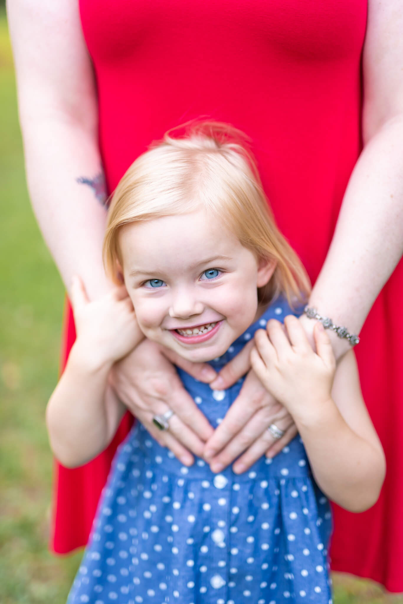 A toddler girl giggles in a blue dress while leaning against mom in a park after finding preschools in savannah ga