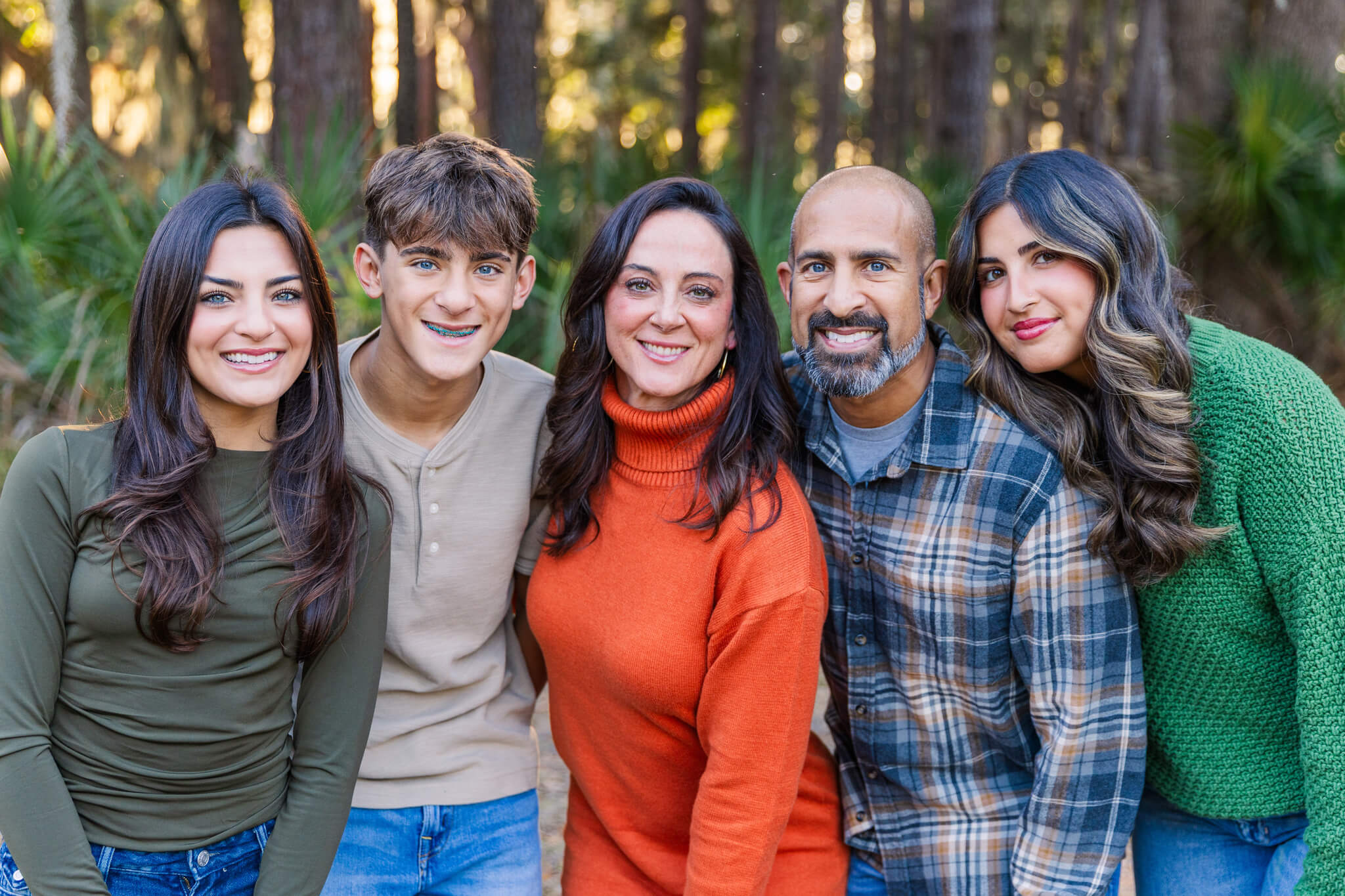 Happy mom and dad stand by a forest with their three teen and adult children at sunset