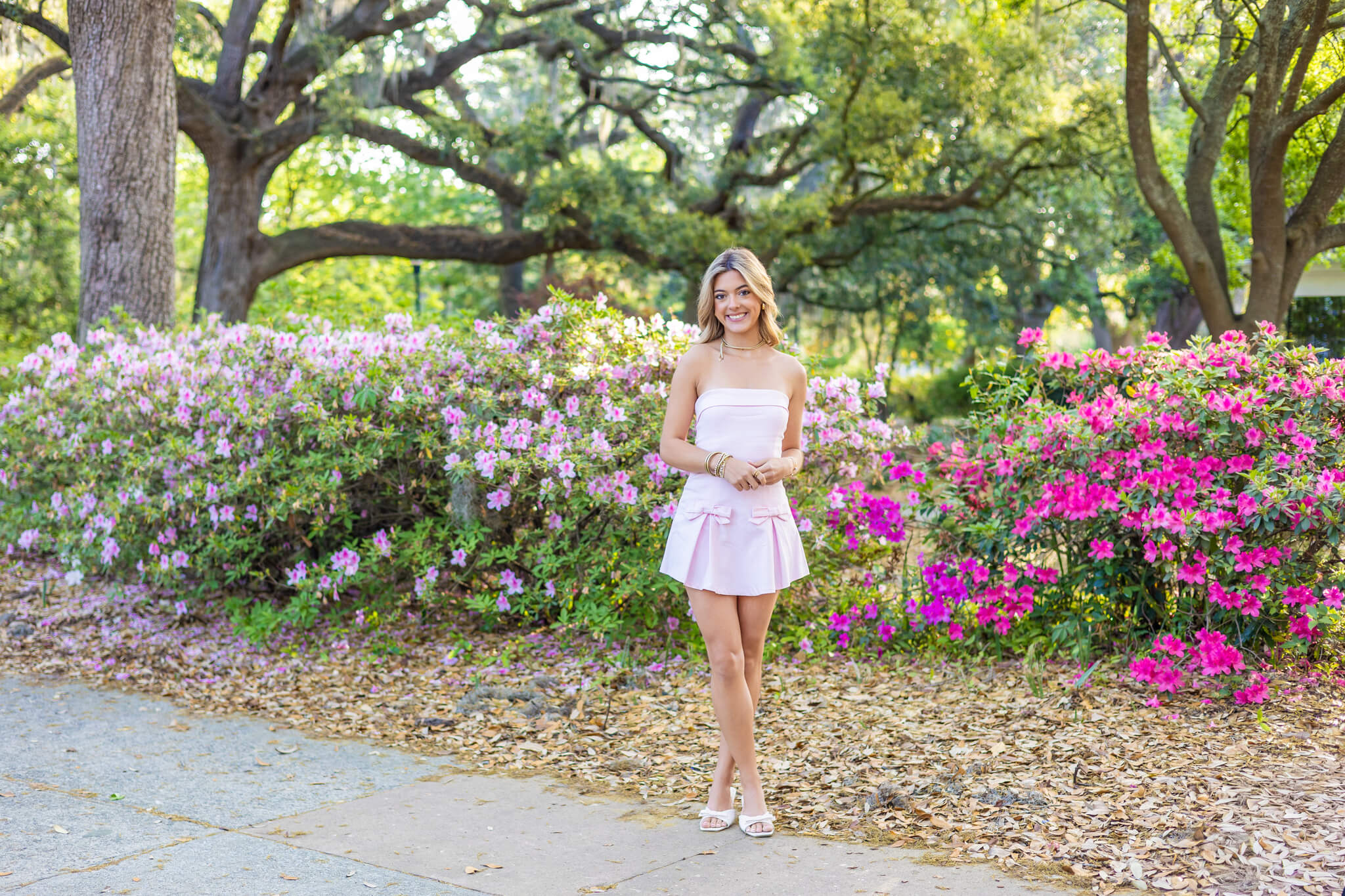 A smiling high school senior stands in a garden pat surrounded by flowering azaleas in a pink dress after finding SAT prep in Savannah, GA
