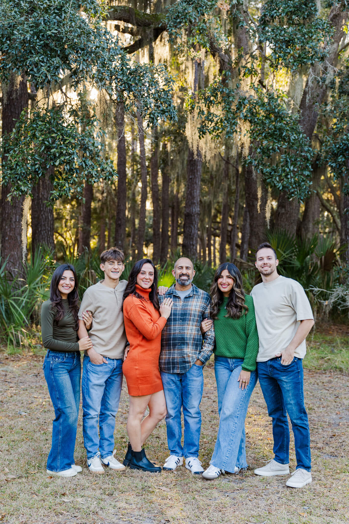 A family of six stand smiling in a park at sunset