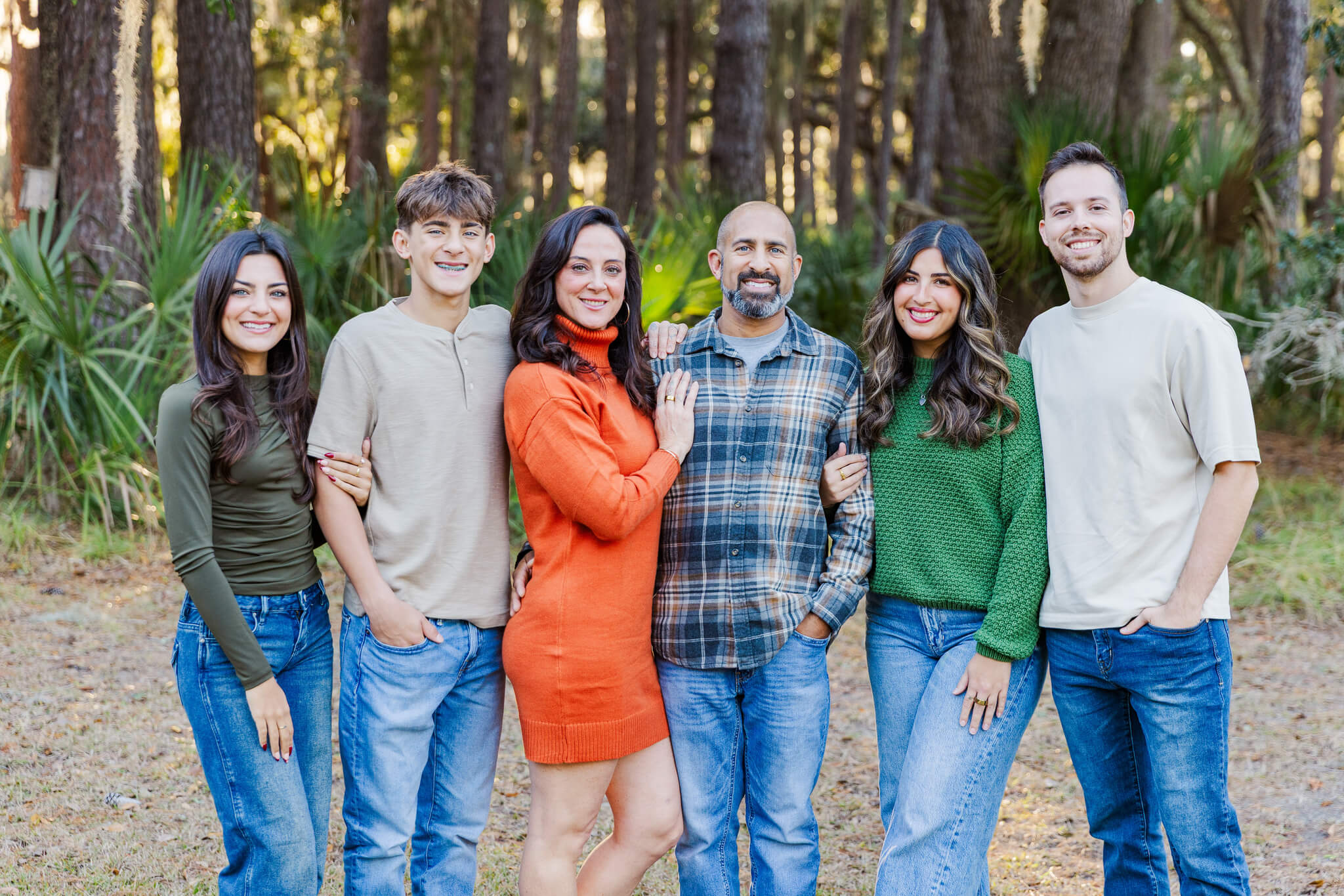 A mom and dad stand with their four adult children in a park in jeans and plaid at sunset after enjoying couples activities in savannah ga
