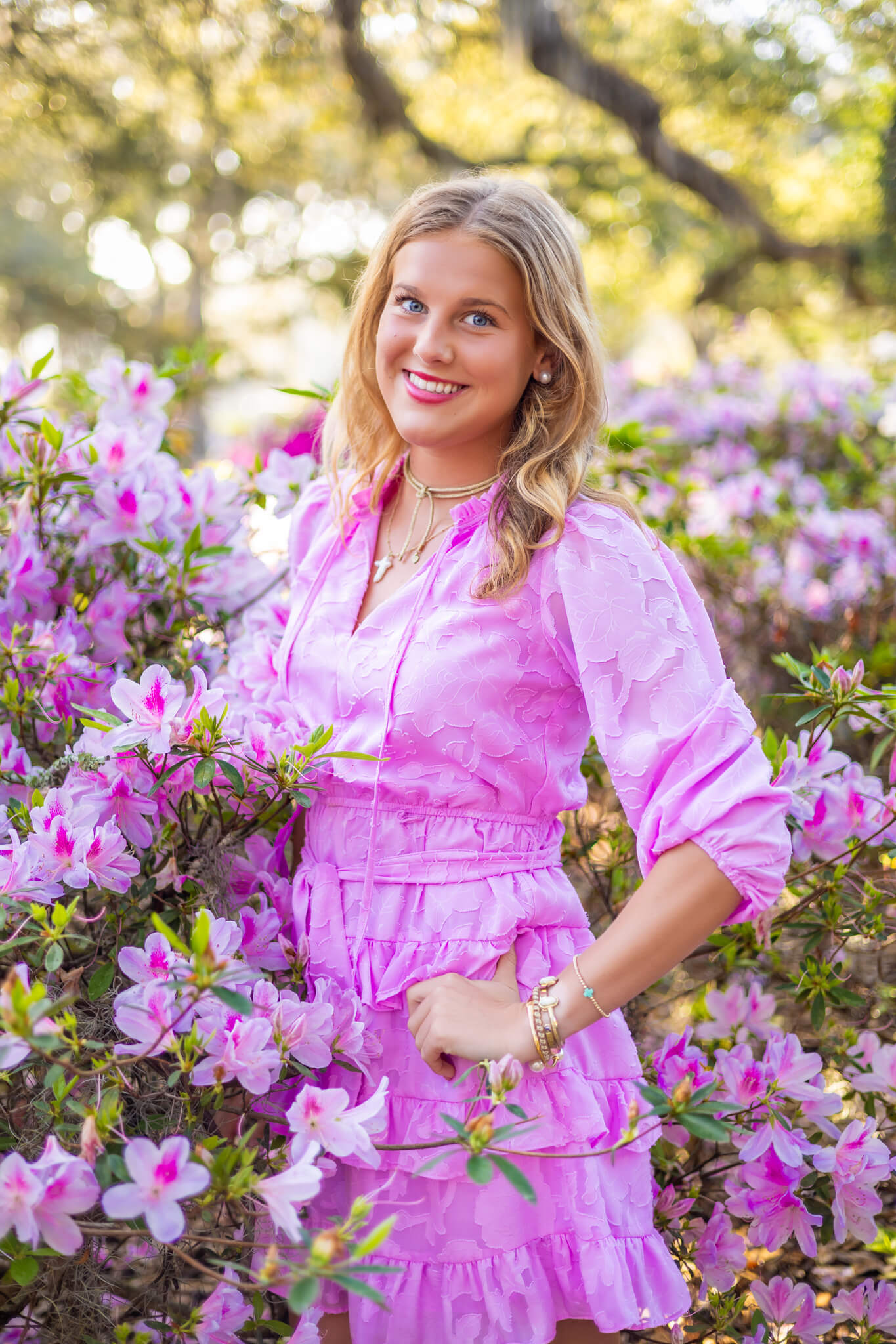 A high school senior with a hand on her hip stands in pink azaleas in a matching pink dress after visiting hair salons in savannah ga