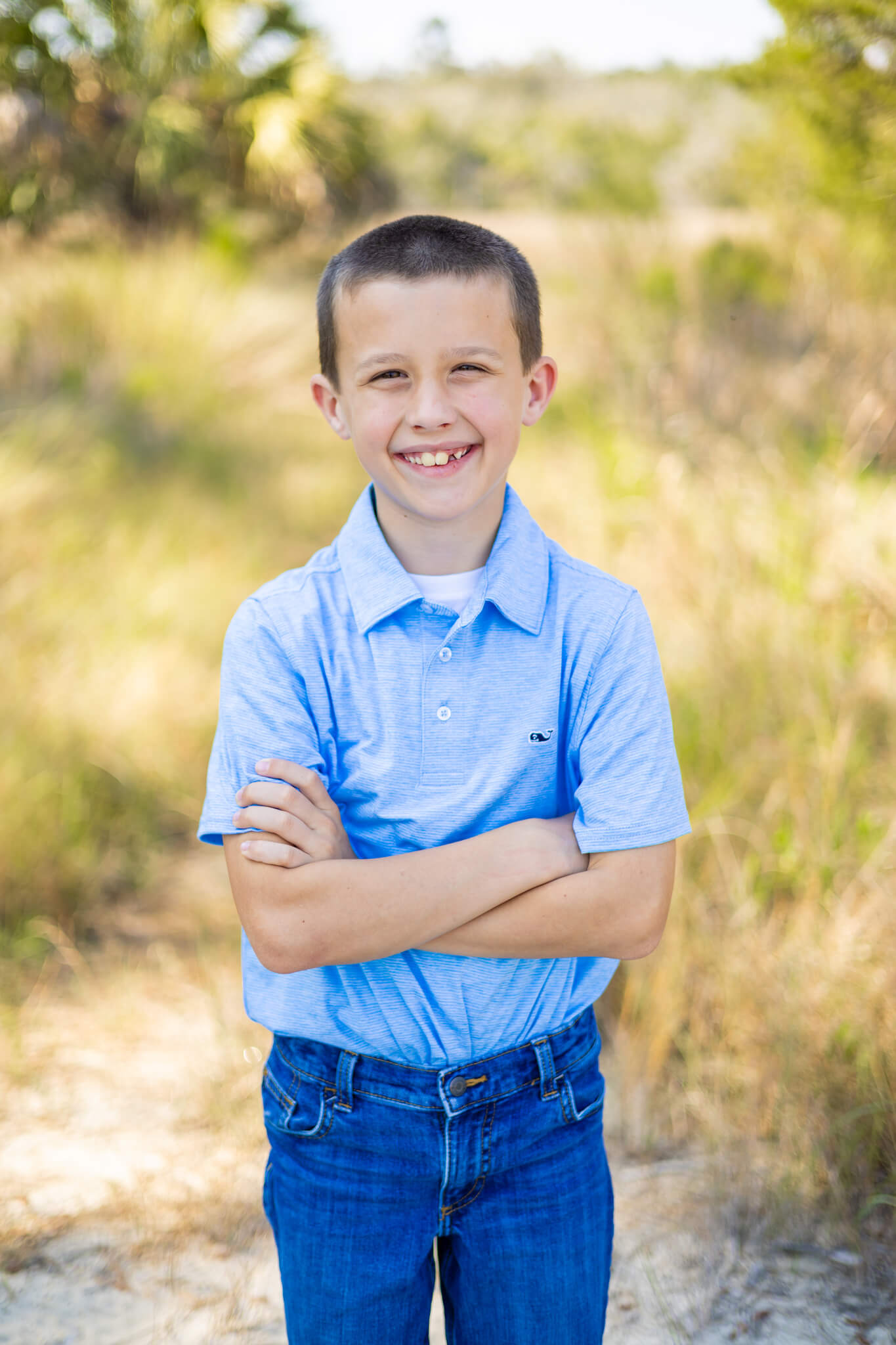A toddler boy stands smiling with arms crossed in a park after visiting pediatric dentists in savannah