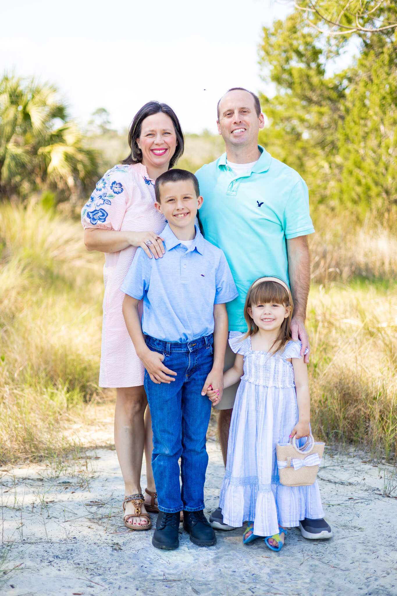 A mom and dad stand smiling in the a sandy trail with their young son and toddler daughter in blue before heading to a romantic bed and breakfast in savannah ga