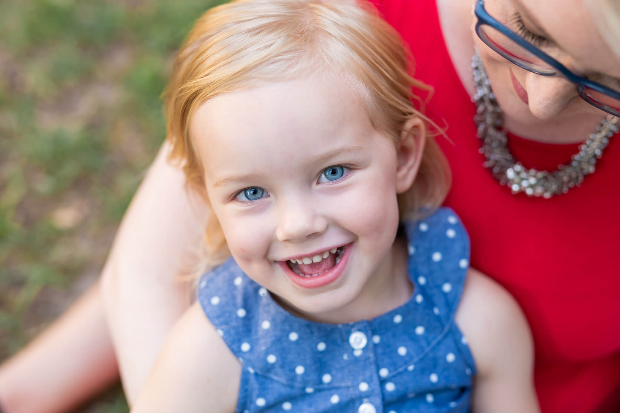 A happy toddler girl in a blue dress giggles while sitting in mom's lap in a park after some swim lessons in savannah ga