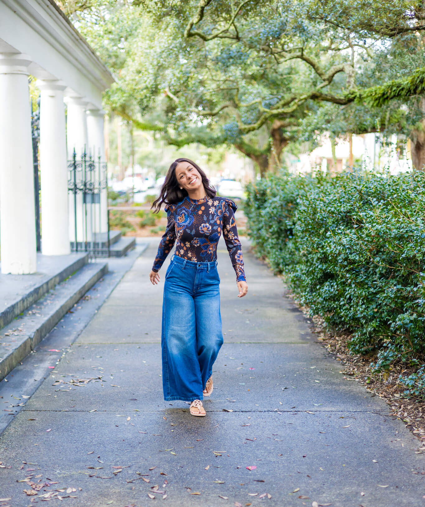 A happy graduate walks in jeans and flower print blouse through a park under live oaks after visiting tanning salons in savannah ga