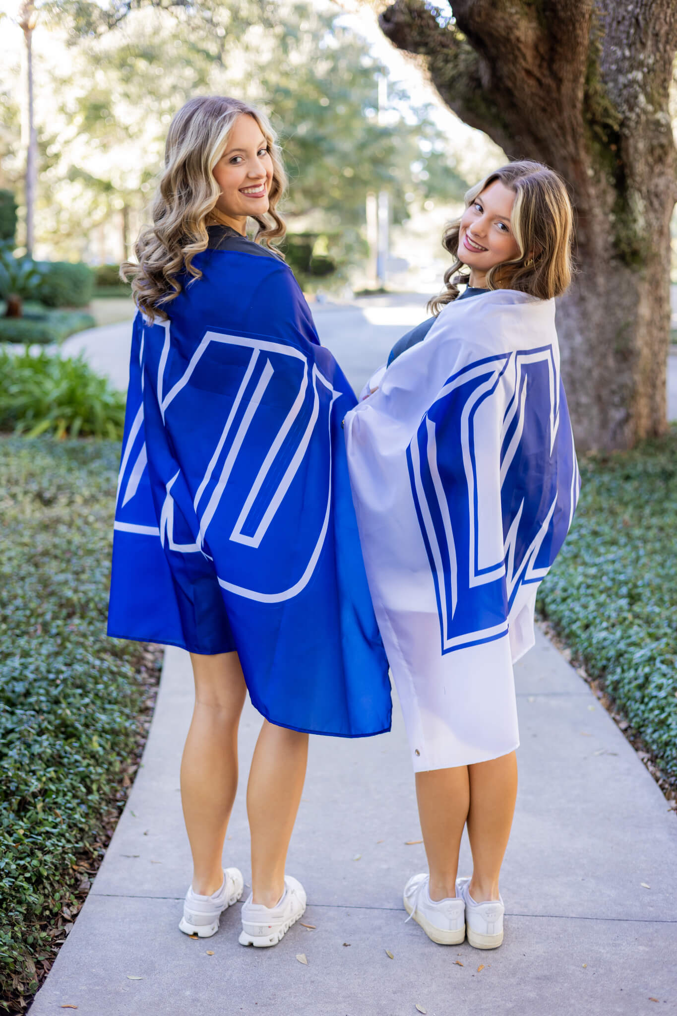 Happy high school seniors wrapped in blue school flags stand in a sidewalk smiling over their shoulders after enjoying volunteer opportunities in Savannah, GA