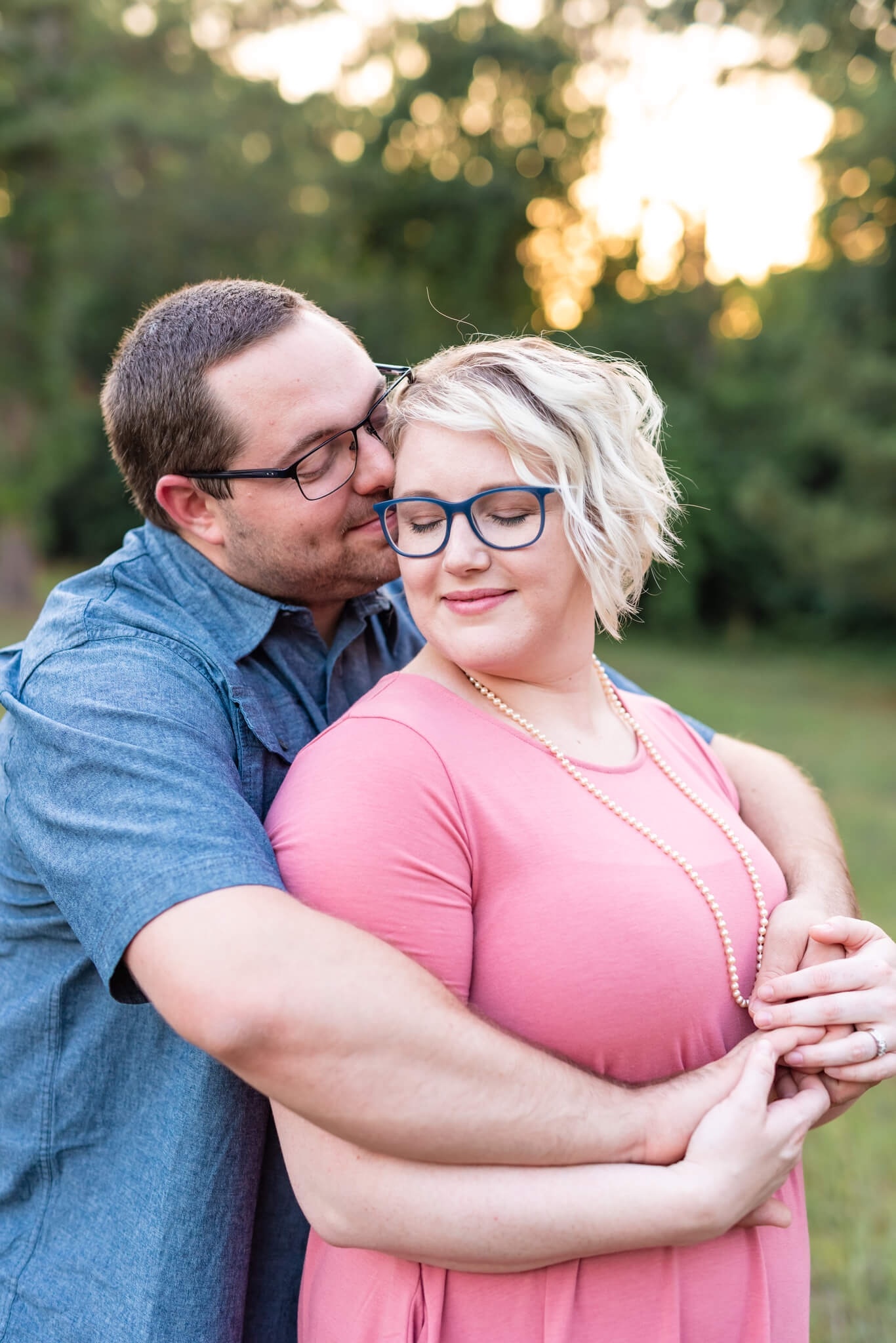 A man hugs his wife from behind as they snuggle standing in a park at sunset before heading to couples cooking classes in savannah, ga