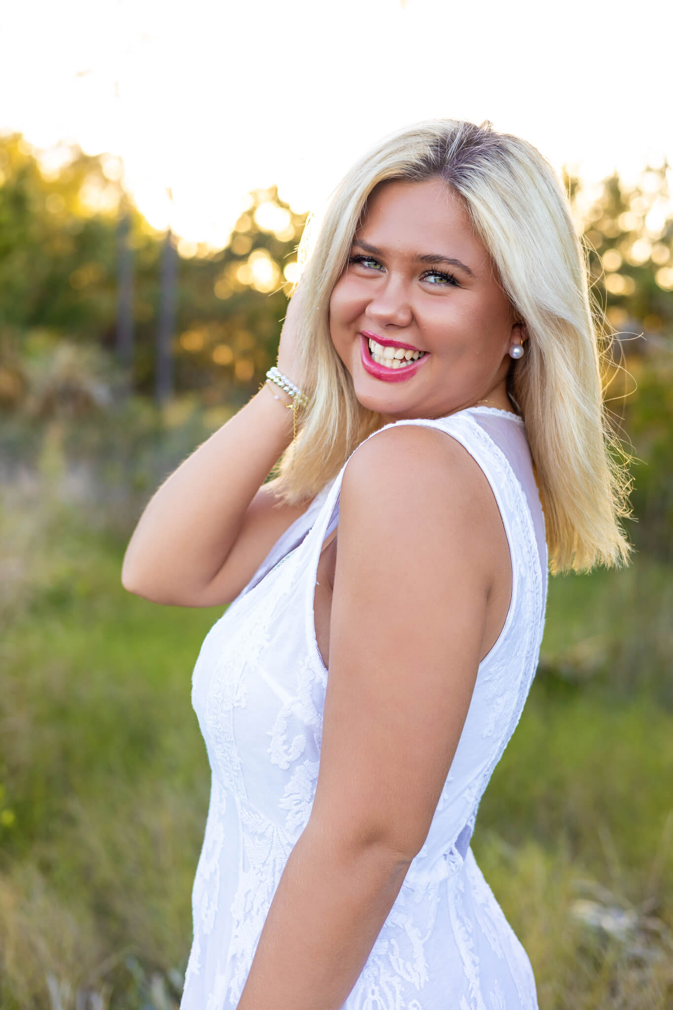 A happy high school senior smiles while turning and playing with her blonde hair in a park at sunset after finding event spaces in savannah, ga for her graduation party