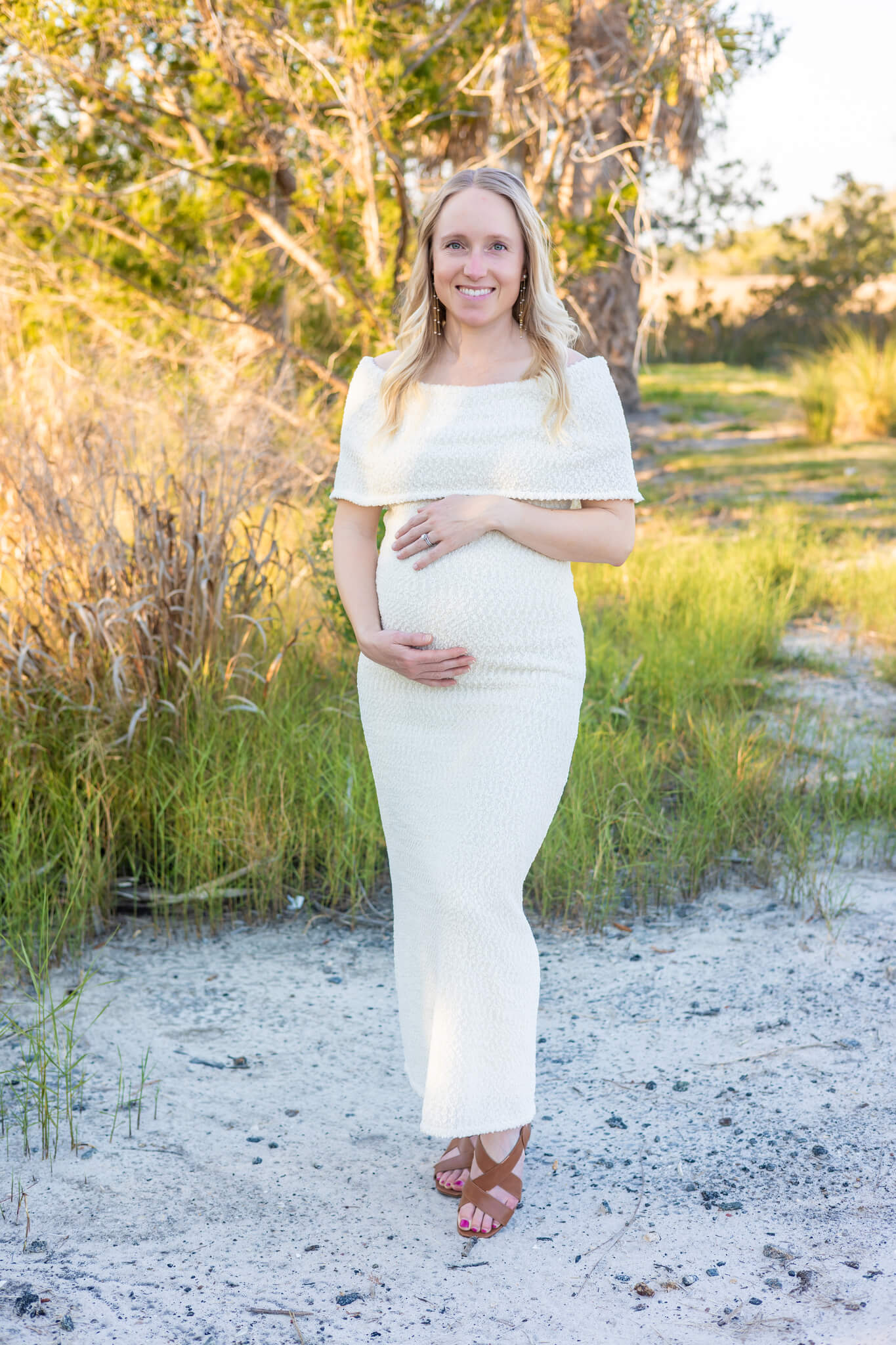 A smiling pregnant woman stands in a yellow dress in a park trail at sunset after enjoying places to propose in savannah, ga