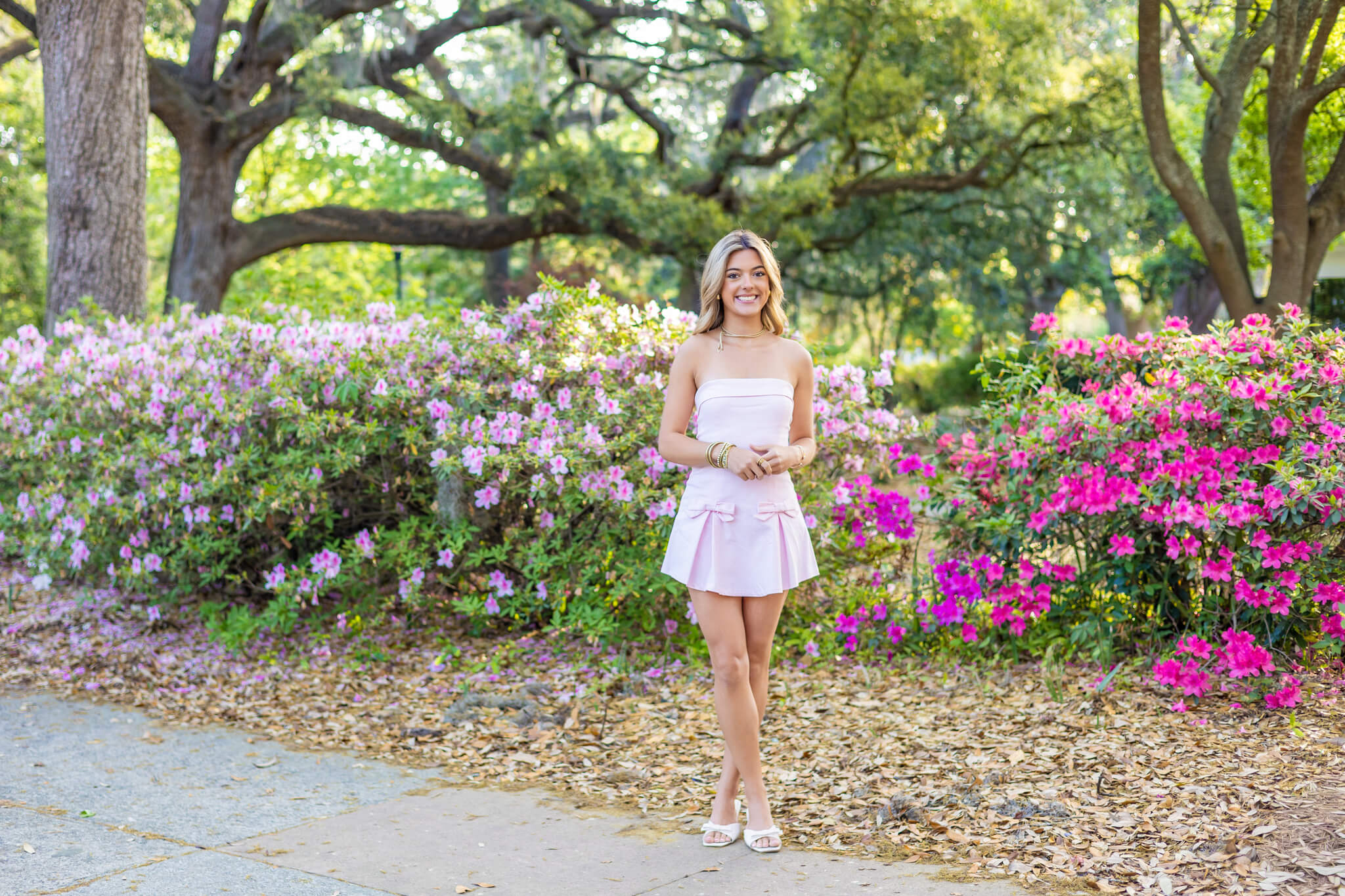A woman smiles while walking in an azalea garden in a pink dress