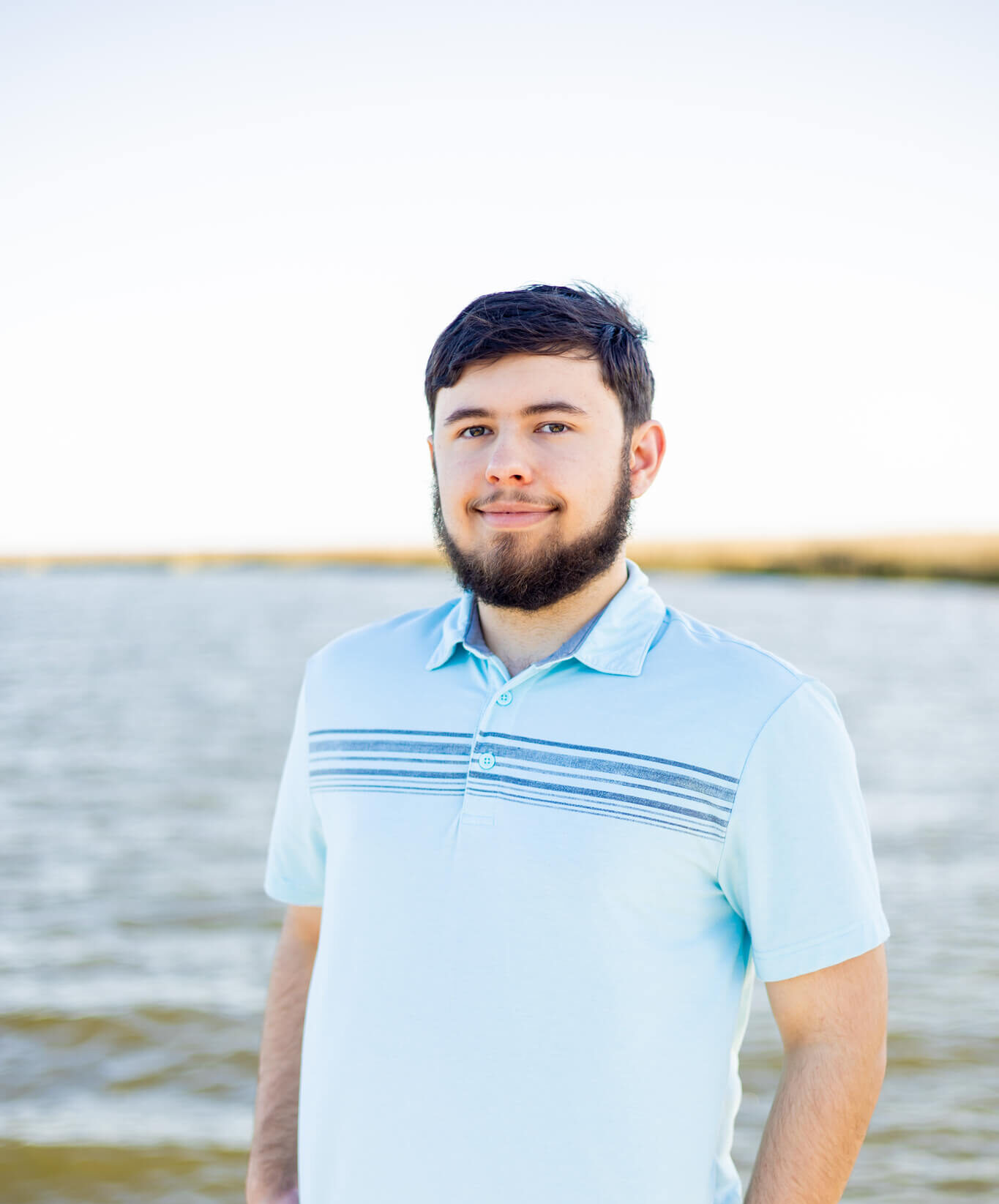 A high school senior in a blue polo stands on a dock with hands in his khaki pockets smiling at sunset after enjoying tutoring in Pooler, GA