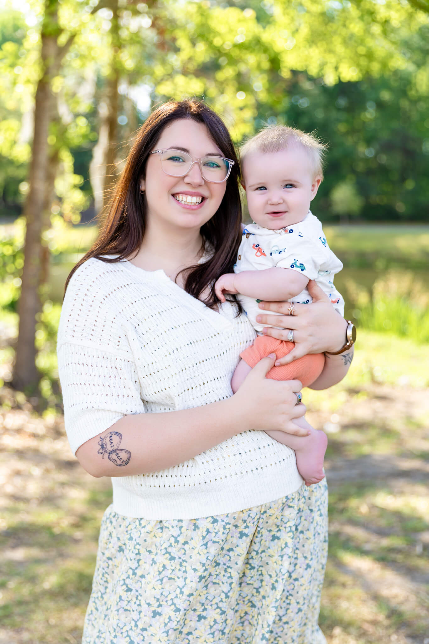 A happy mother in a white sweater smiles big while holding her baby boy in her arms in a park