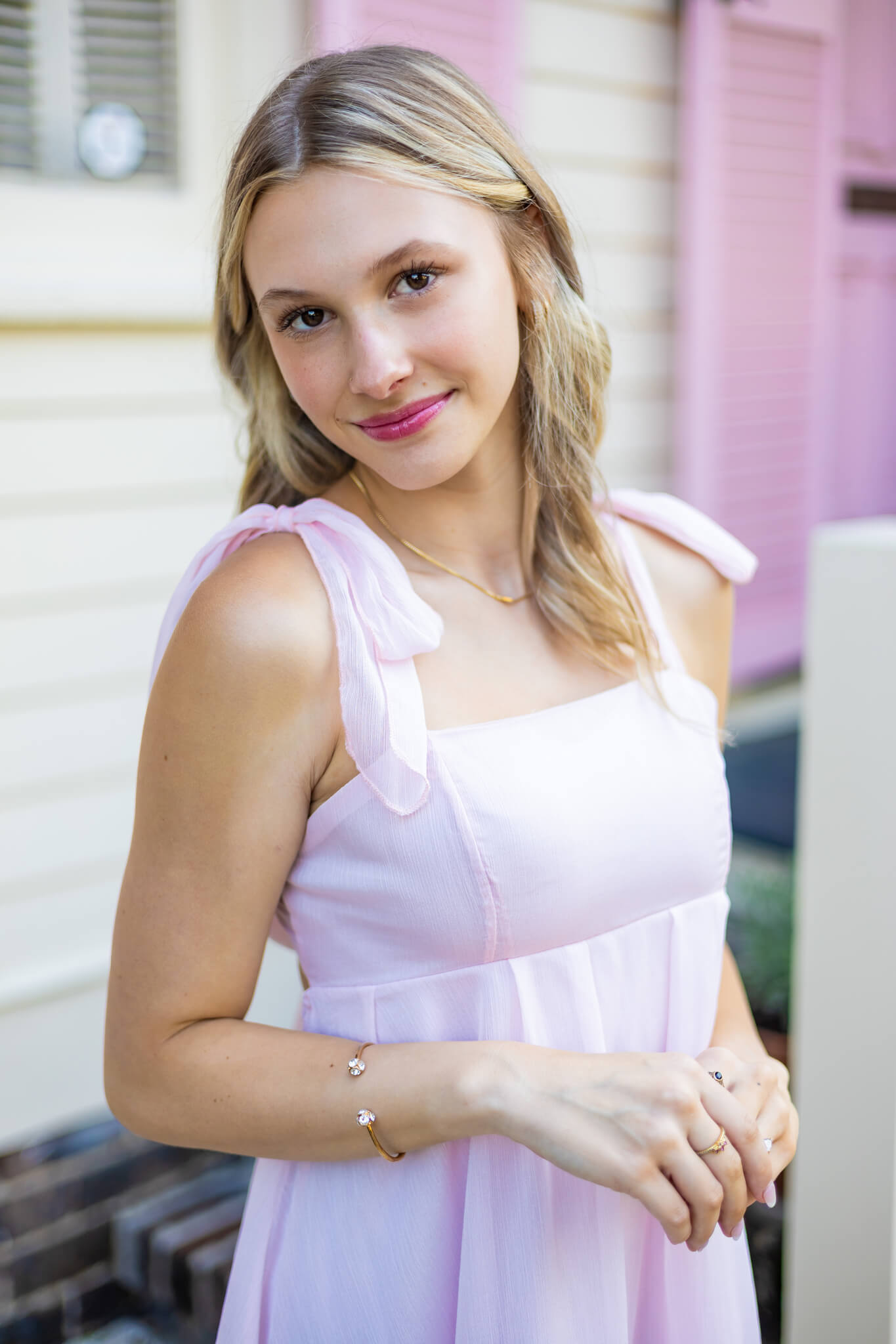 A smiling high school senior in a pink dress standing in front of a pink building after visiting nail salons in pooler ga