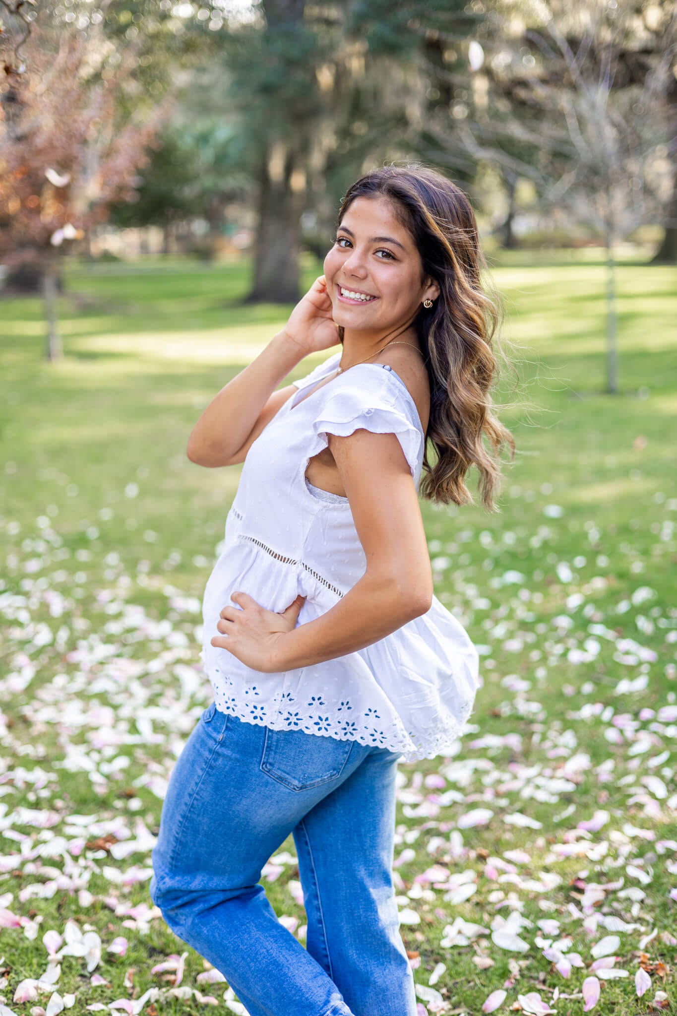 A happy woman walks and smiles in a park lawn in a white blouse and jeands