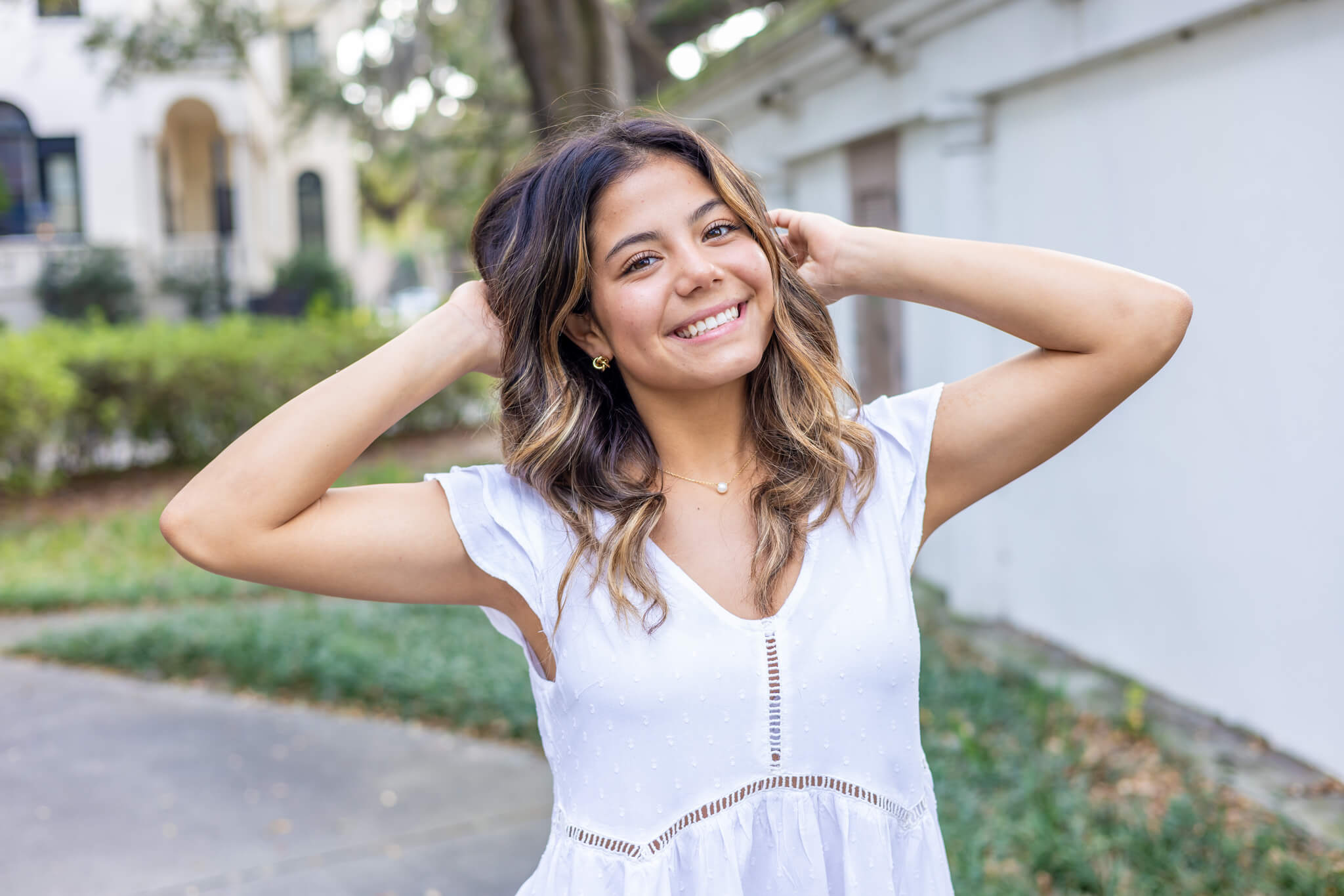 A smiling high school senior with hands in her hair walks in a white dress after visiting boutiques in Richmond Hill, GA