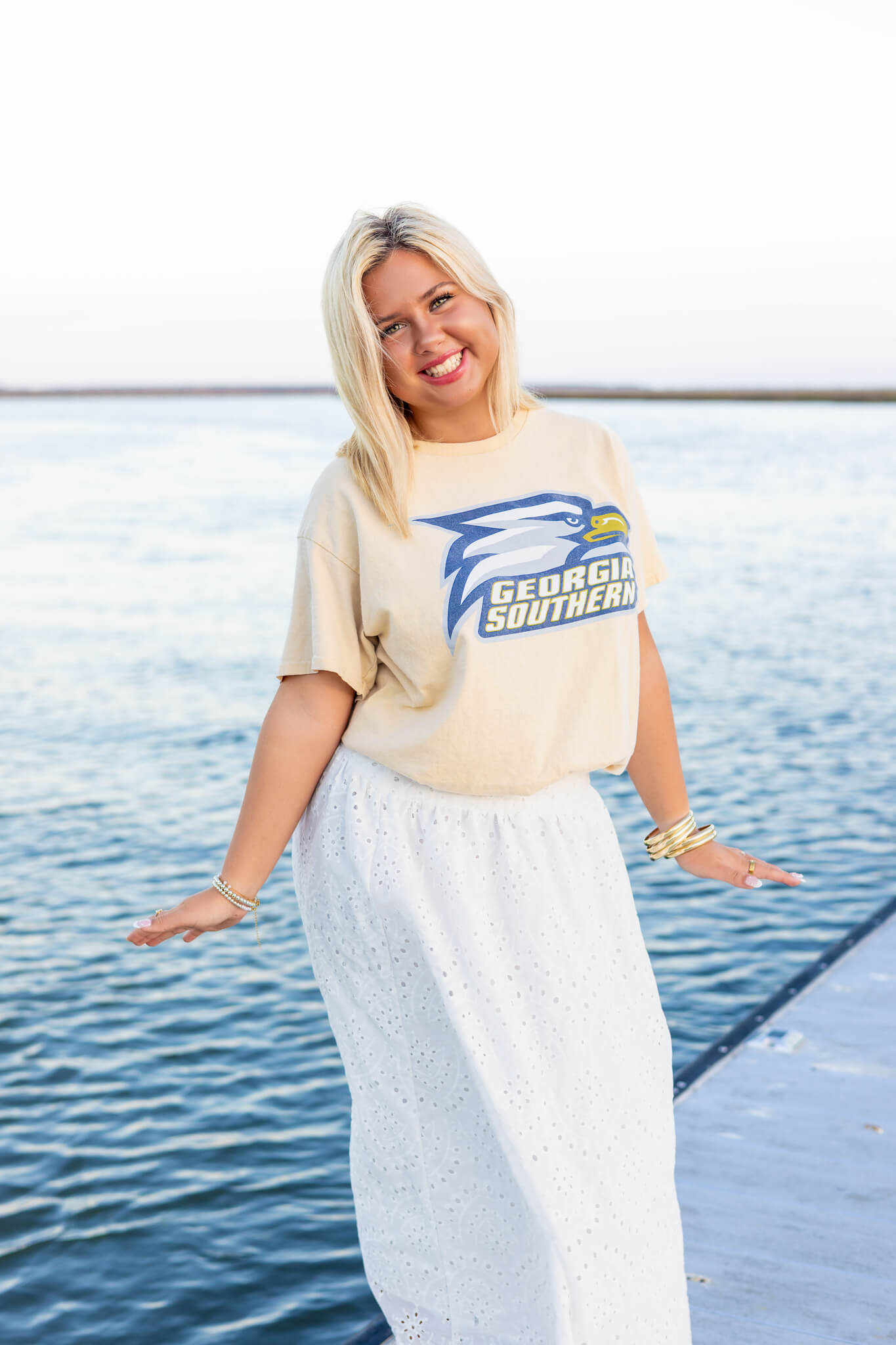 A happy woman in a yellow shirt and white skirt plays on a dock after exploring colleges near pooler ga