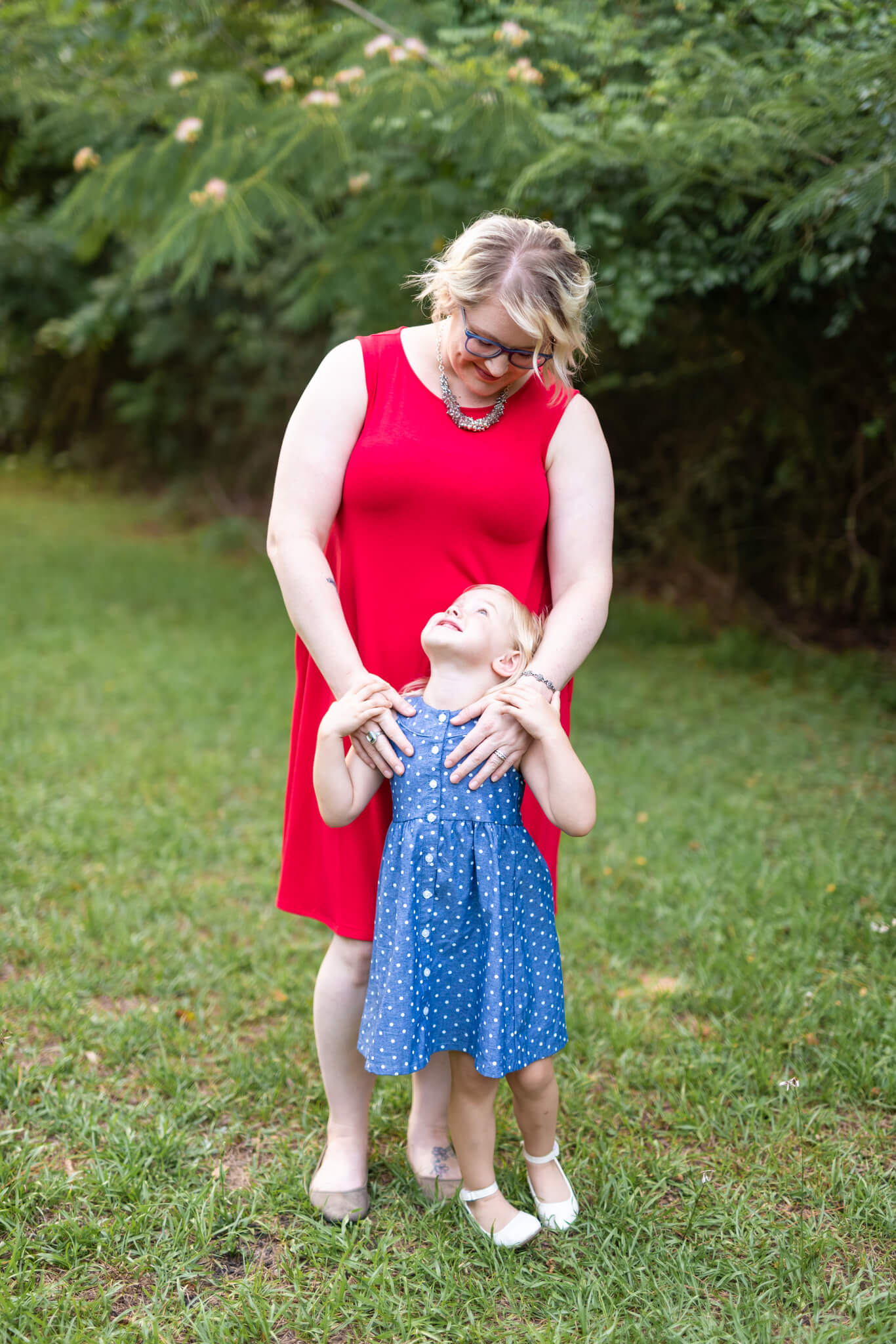 A happy mom in a red dress smiles down to her happy toddler daughter in a blue dress before visiting a day spa in pooler ga