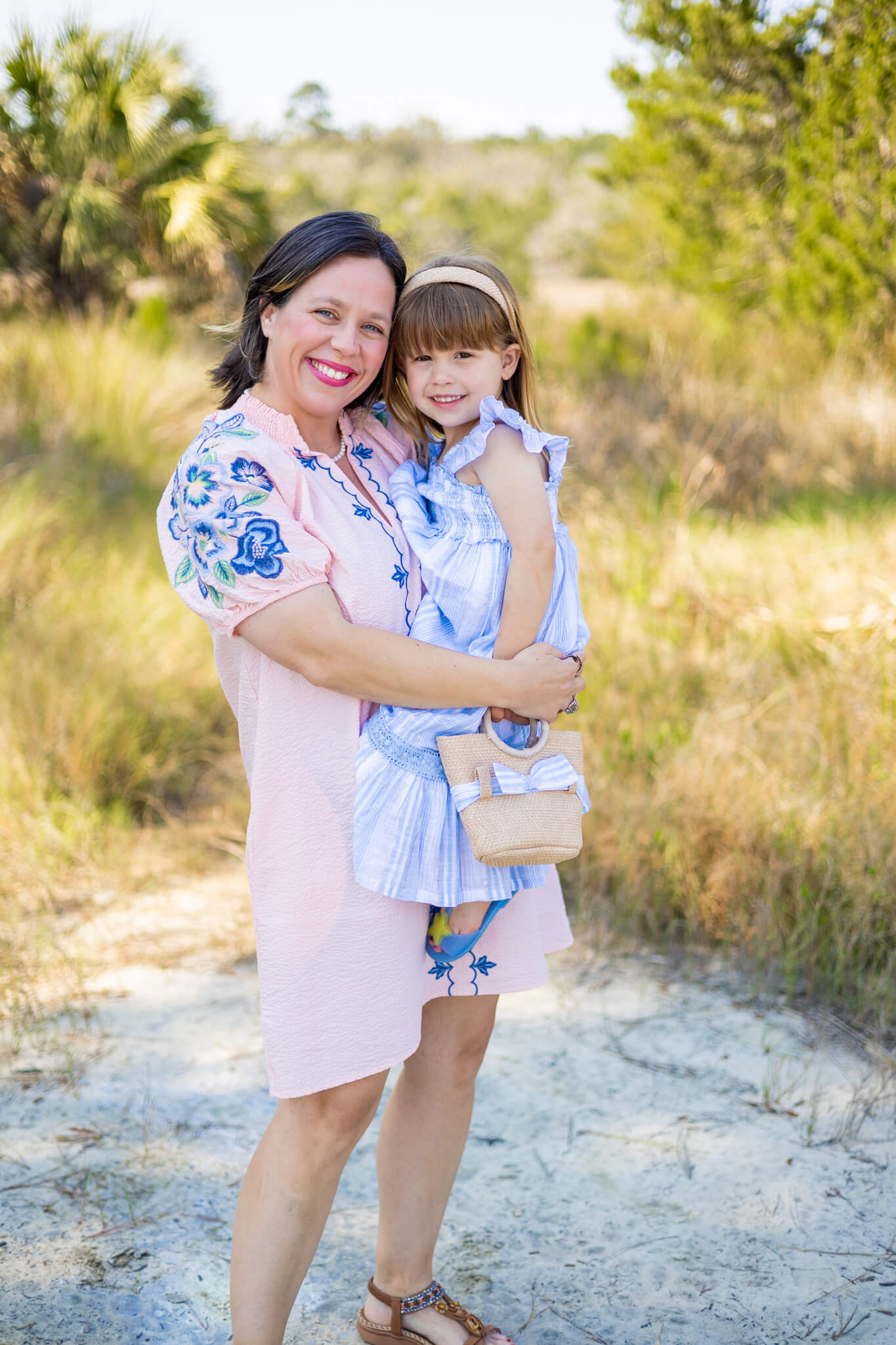 A happy mother in a pink dress holds her toddler daughter in a blue dress in a park at sunset after some marriage counseling in richmond hill, GA