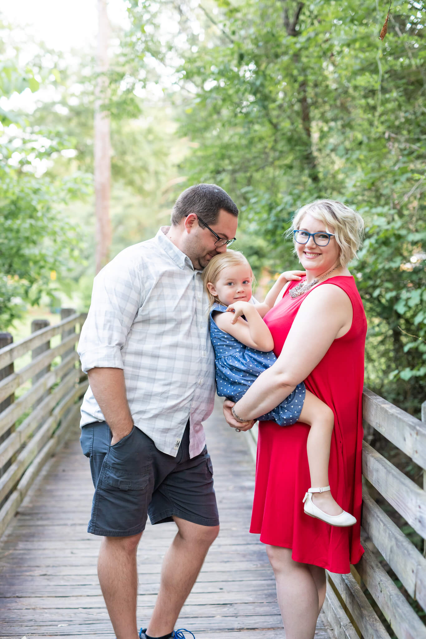 Mom and dad hold their toddler daughter while standing on a park boardwalk after enjoying a couples massage in richmond hill ga