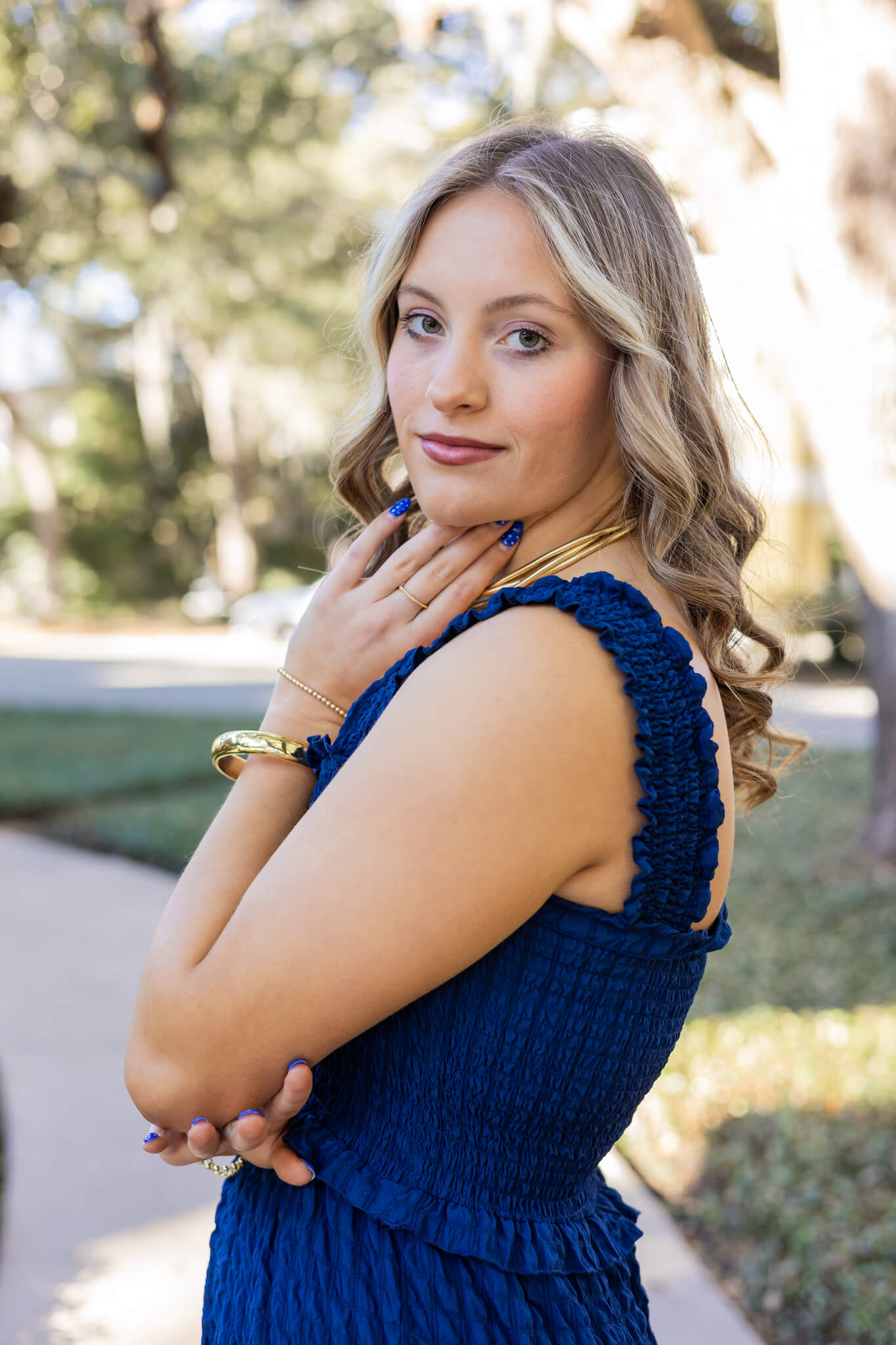 A high school senior in a blue dress and matching nails under her chin stands in a park garden after visiting nail salons in richmond hill ga