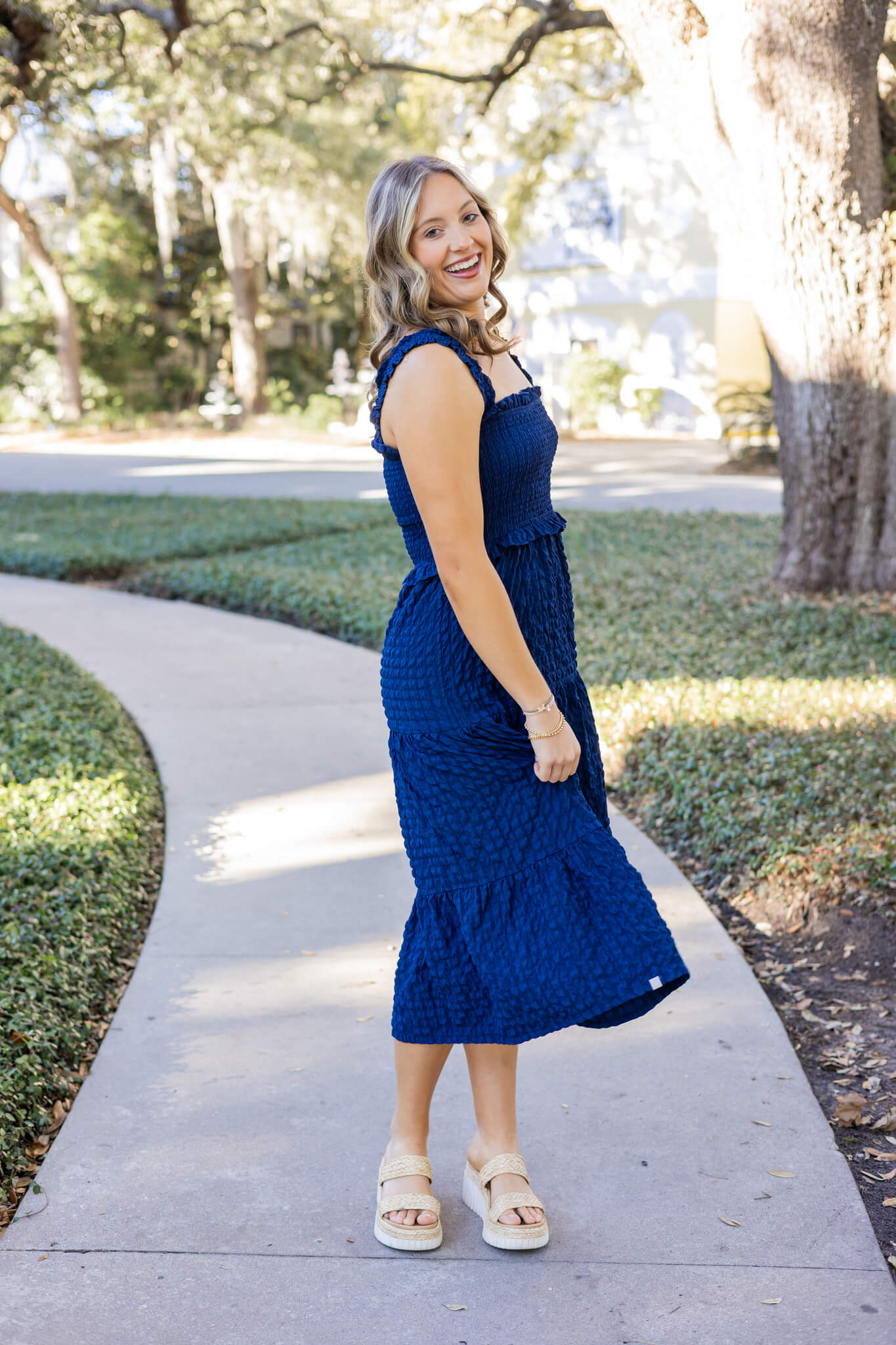 A woman in a blue dress twirls in a park sidewalk with a big smile