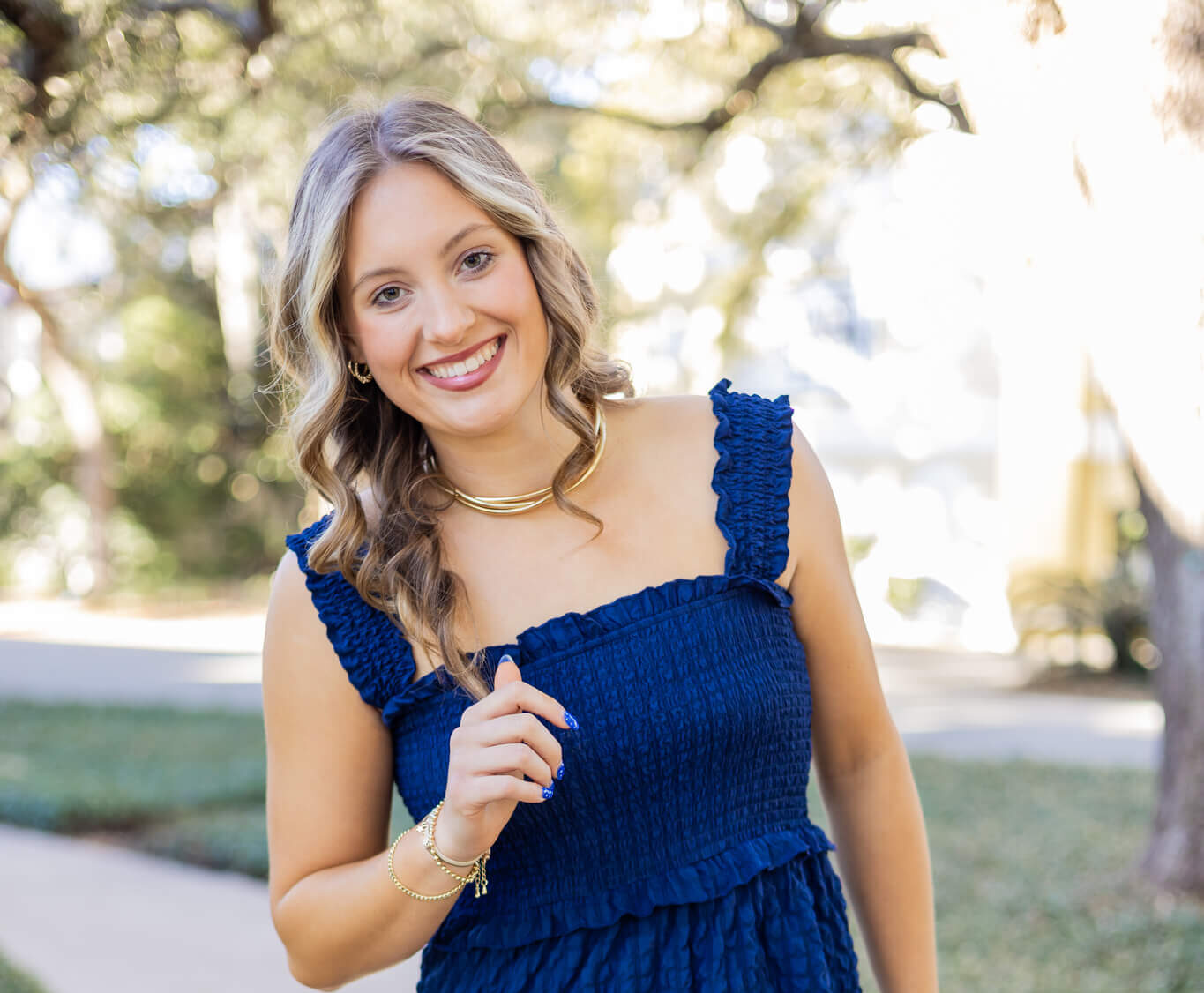 A happy high school senior in a blue dress and matching nails walks in a park sidewalk after visiting nail salons in richmond hill ga